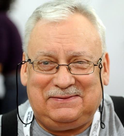 Portret Andrzeja Sapkowskiego z elementami świata Wiedźmina w tle.