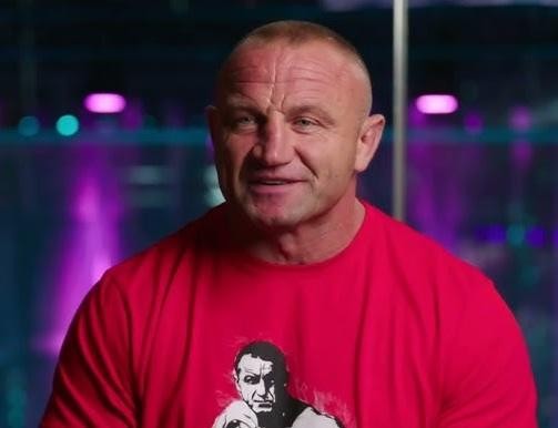 Mariusz Pudzianowski w dynamicznej akcji w klatce MMA, prezentujący siłę i skupienie podczas walki.