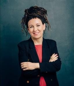 Dłonie Olgi Tokarczuk trzymające otwartą książkę w przytulnym wnętrzu, symbolizujące jej pasję do literatury.