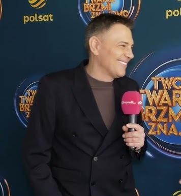 Krzysztof Ibisz prowadzący dynamicznie teleturniej telewizyjny w studiu.