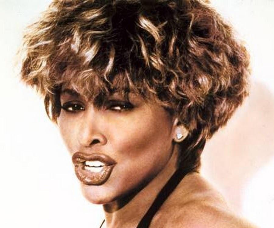 Tina Turner śpiewająca z pasją na koncercie, z dynamicznym oświetleniem scenicznym.